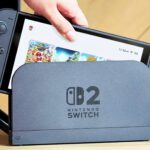 nintendo switch 2 being loaded into a dock with the home screen visible as it s being placed inside