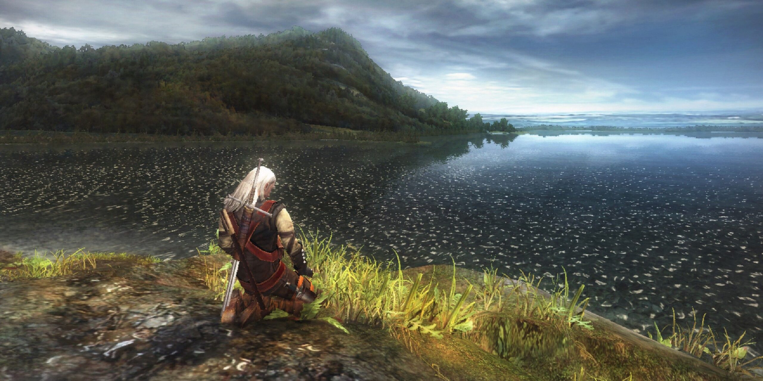 screenshot from the witcher of a white haired character kneeling in front of a beautiful lakeside.jp scaled