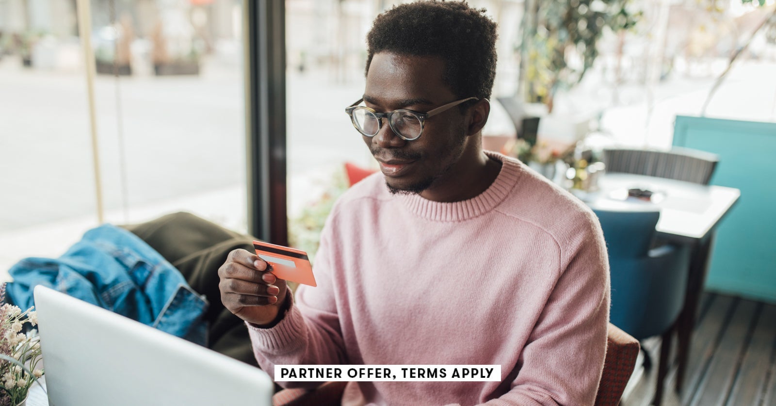 SOCIAL IMAGE PARTNER OFFERS TERMS APPLY Man sitting at cafe using laptop and holding credit