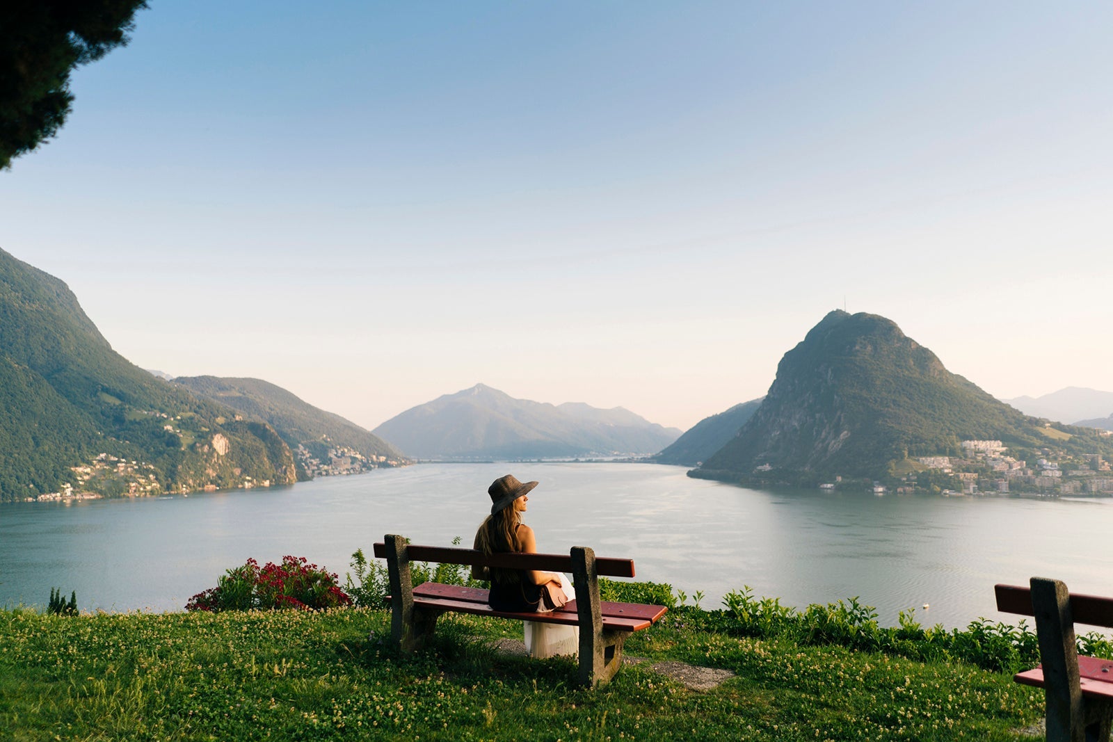 Woman relaxes on bench looking over lake and mountains in Switzerland AscentXmedia