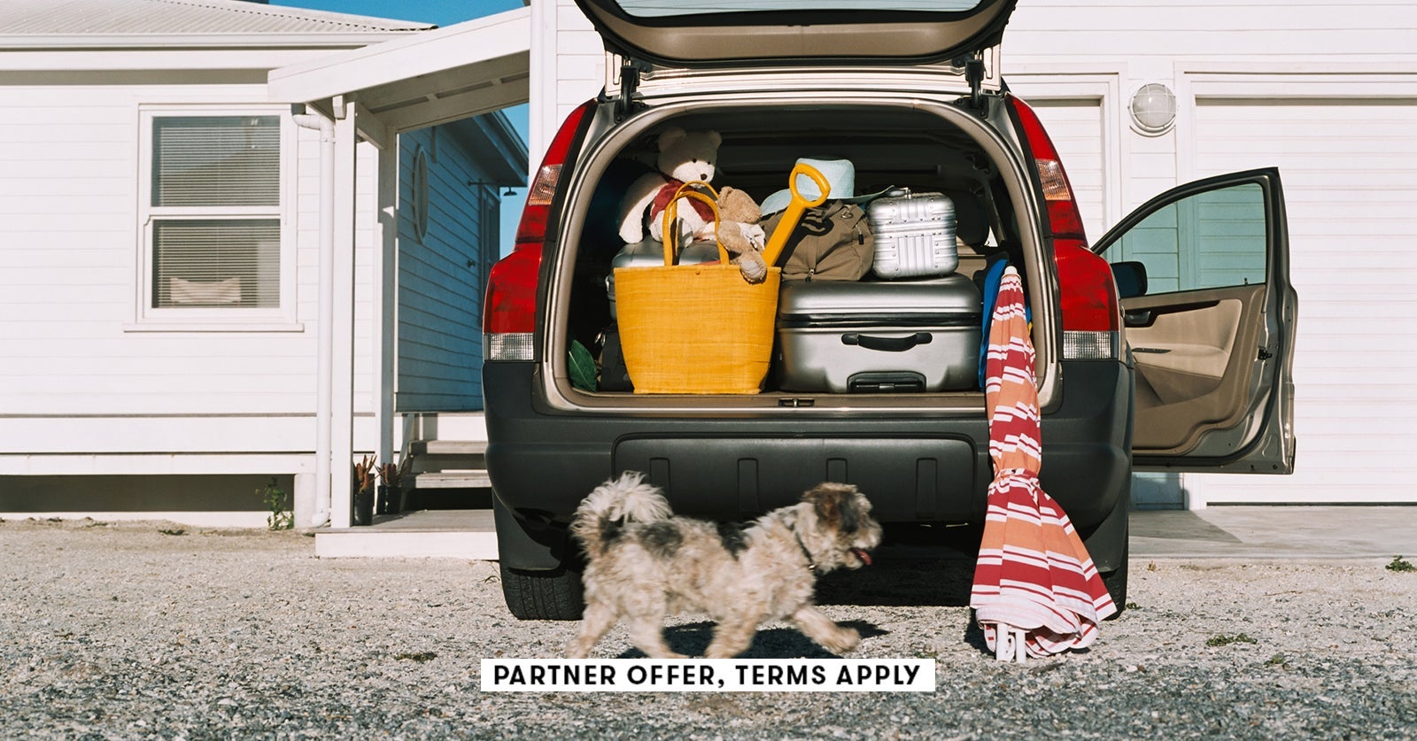 SOCIAL IMAGE PARTNER OFFER TERMS APPLY Dog running by car full of luggage for summer roadtrip Image